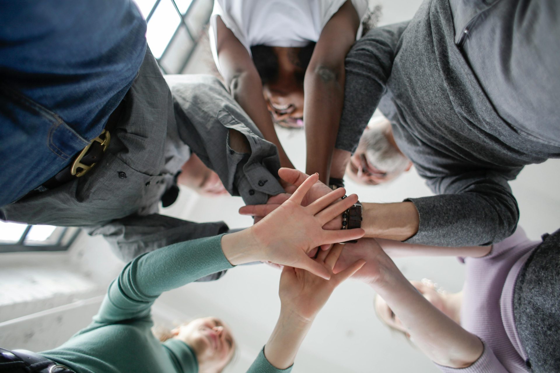 Low angle view of a diverse group uniting hands indoors, symbolizing teamwork and collaboration.