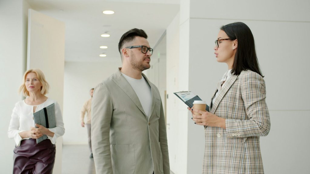 Two colleagues talking in a modern office hallway.